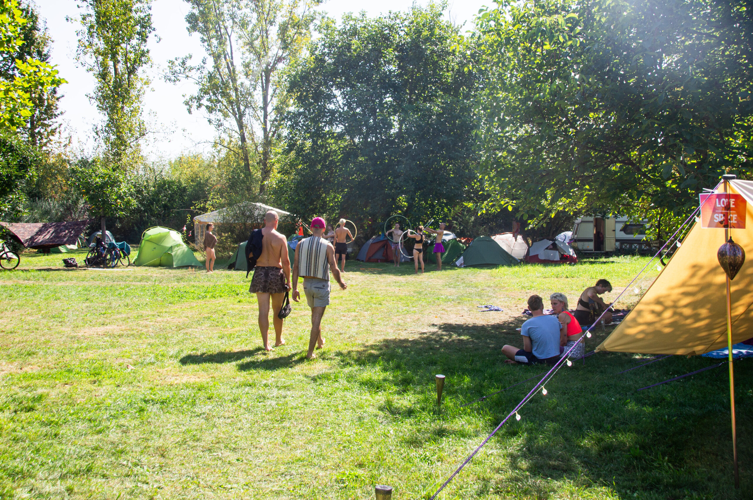 Der Garten. Menschen flanieren in der Sonne und im Schatten, rechts das Love tent, hinten sind einige Zelte.
