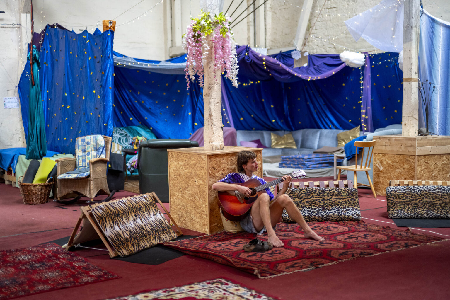 Eine Person sitzt mit Gitarre in der Mitte des Bildes, mensch sieht die Scheune