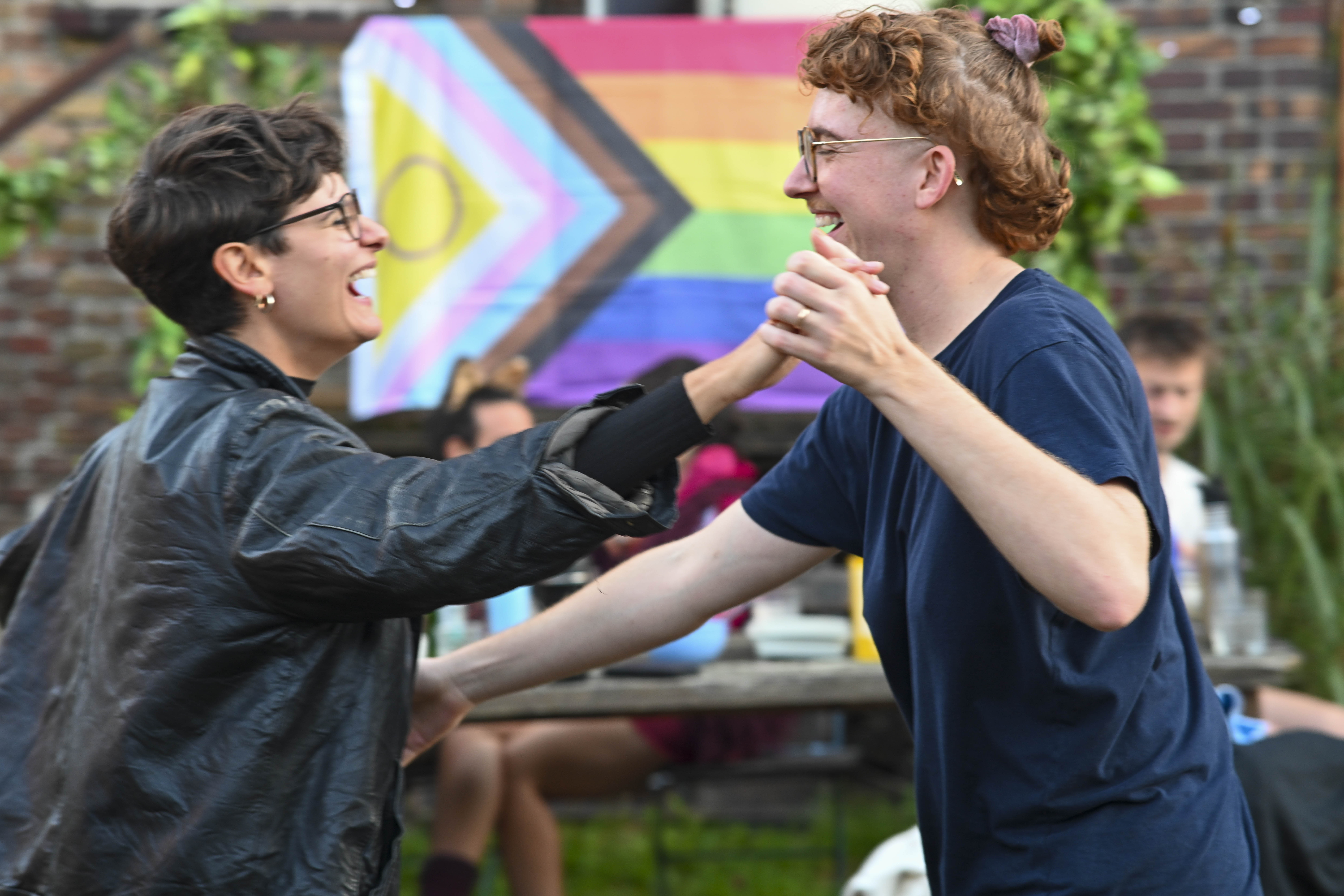 Zwei tanzende Queers vor einer Pride Flag